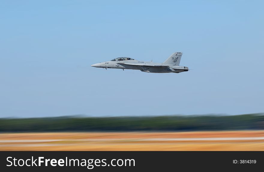 Navy jet plane flying low to the ground showing motion blur to the ground