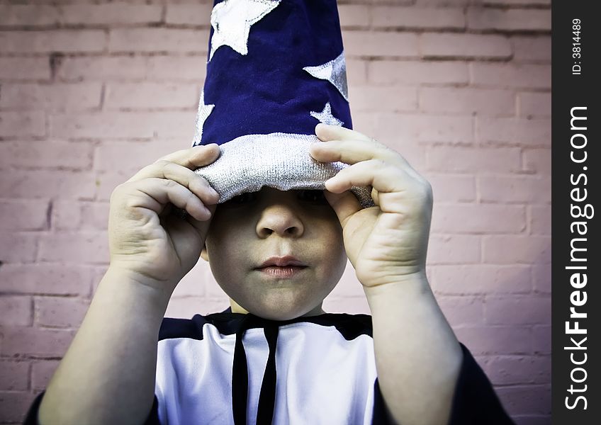 Young boy lifts the brim of a wizard hat and peers out. Young boy lifts the brim of a wizard hat and peers out.