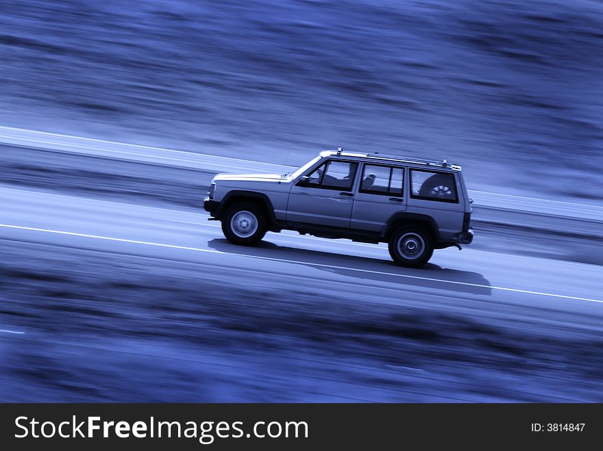 Four door SUV driving along road with blurred background