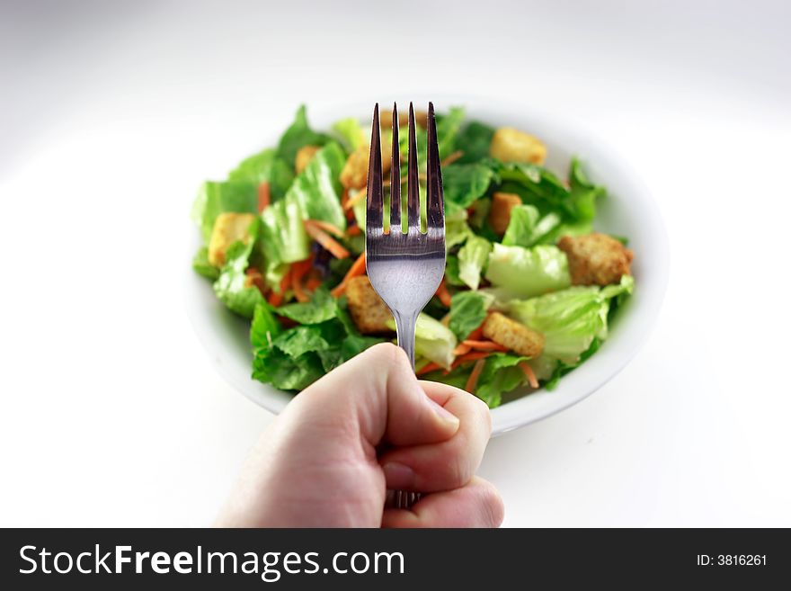 Hand holding fork over generic out of focus salad. Hand holding fork over generic out of focus salad.