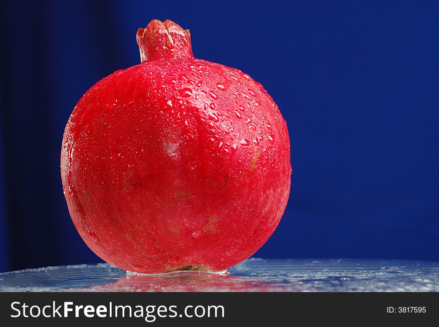 Pomegranate on the glass table over blue background. Pomegranate on the glass table over blue background.
