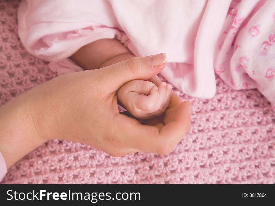 Close up of hands of mother and newborn , baby dressed in pink on a pink knitted background. Close up of hands of mother and newborn , baby dressed in pink on a pink knitted background