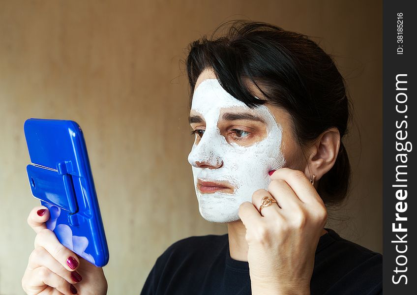 Young beautiful woman gets cosmetic mask in the mirror