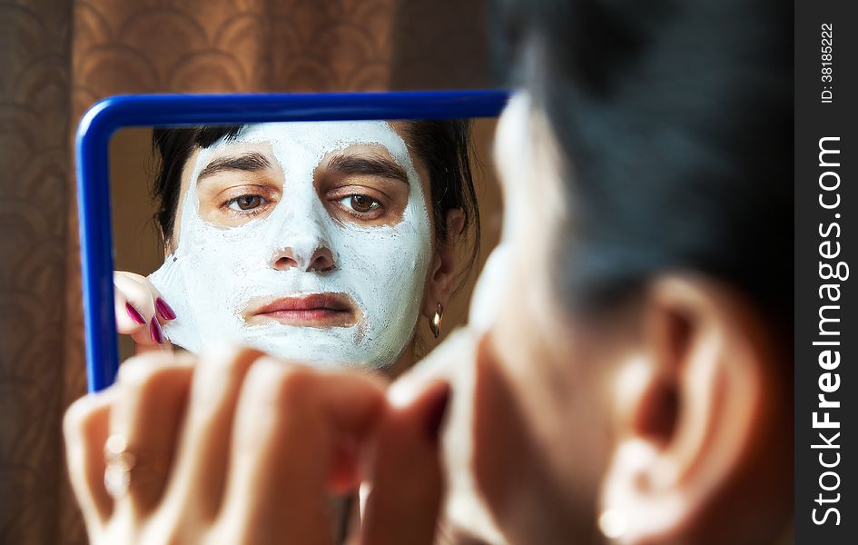 Young woman takes beauty mask in front of mirror