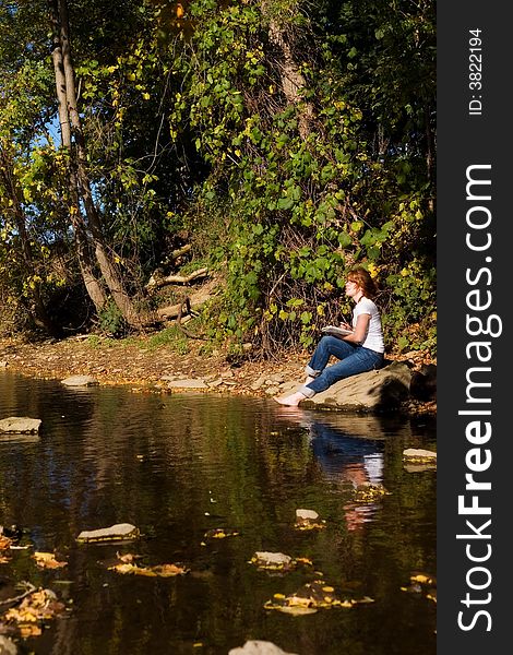 Young woman sketching by a lake. Young woman sketching by a lake.