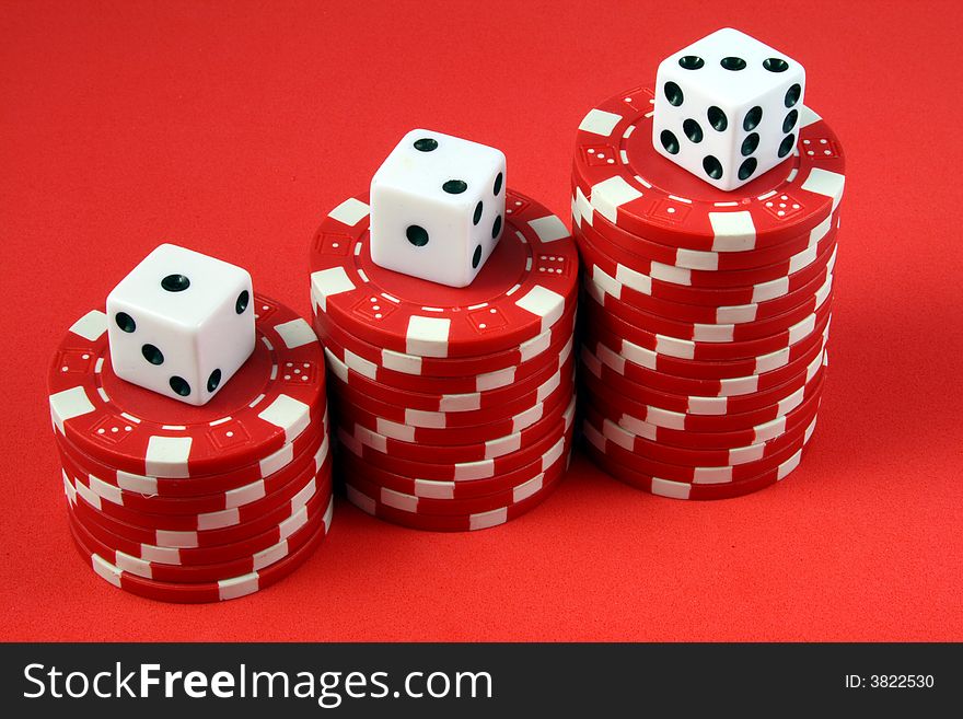 Three piles of red gambling chips with a die on top. Three piles of red gambling chips with a die on top