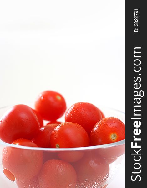 Cherry tomatoes in a transparent glass bowl on a white table-top