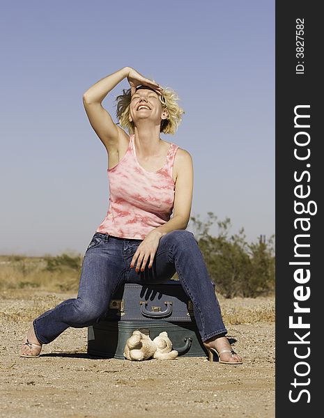 Blonde woman sitting on suitcases and laughing. Blonde woman sitting on suitcases and laughing.