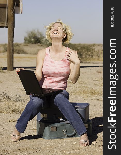 Laughing blonde woman sitting on suitcases outdoors with a laptop computer. Laughing blonde woman sitting on suitcases outdoors with a laptop computer.