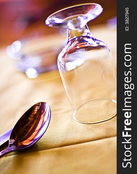 A closeup view of an upside-down drinking glass and a spoon nearby on a table.  . A closeup view of an upside-down drinking glass and a spoon nearby on a table.