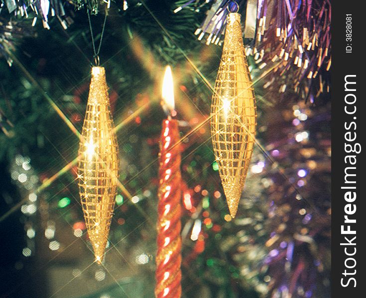 Burning candle between two fur-tree toys in the form of icicles. Burning candle between two fur-tree toys in the form of icicles