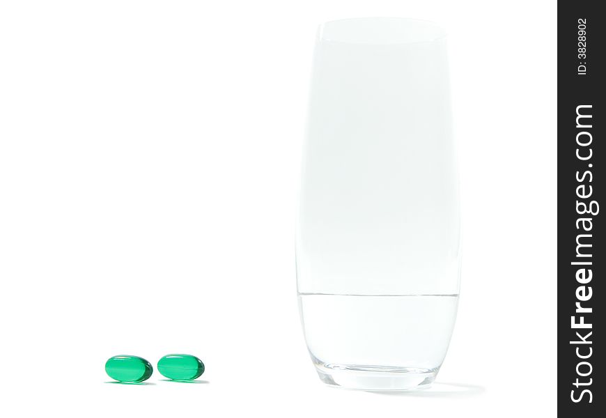 Green soft gel pills and a glass with water isolated on white background