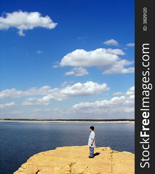 A young boy standing on a cliff at a reservoir looking at the clouds. A young boy standing on a cliff at a reservoir looking at the clouds.