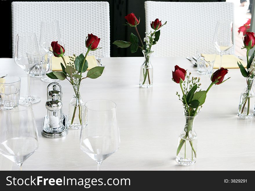 Elegant table setting with vases of red roses and white linen.