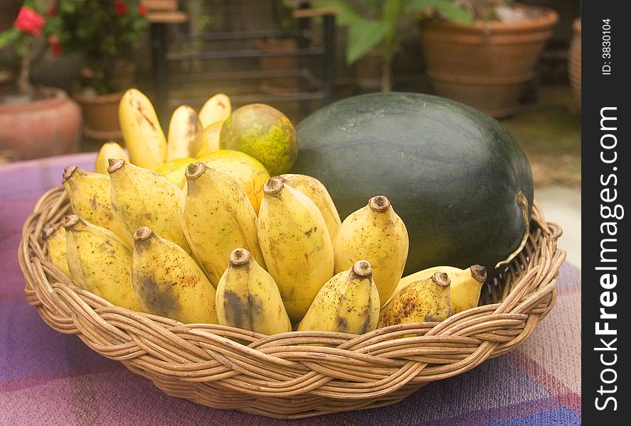 Basket with assorted, tropical fruit, bananas, watermelon and oranges, on a table in a garden. Basket with assorted, tropical fruit, bananas, watermelon and oranges, on a table in a garden.