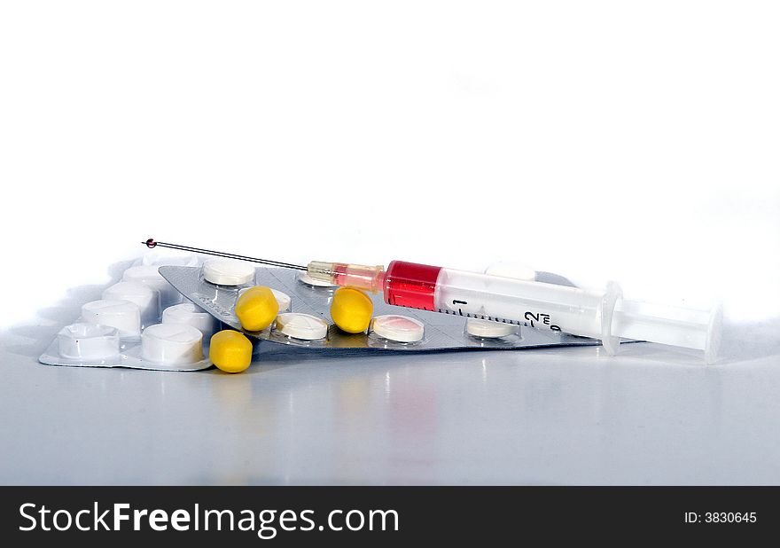 A syringe filled with liquid and different pills. Isolated over white space (for text). A syringe filled with liquid and different pills. Isolated over white space (for text).