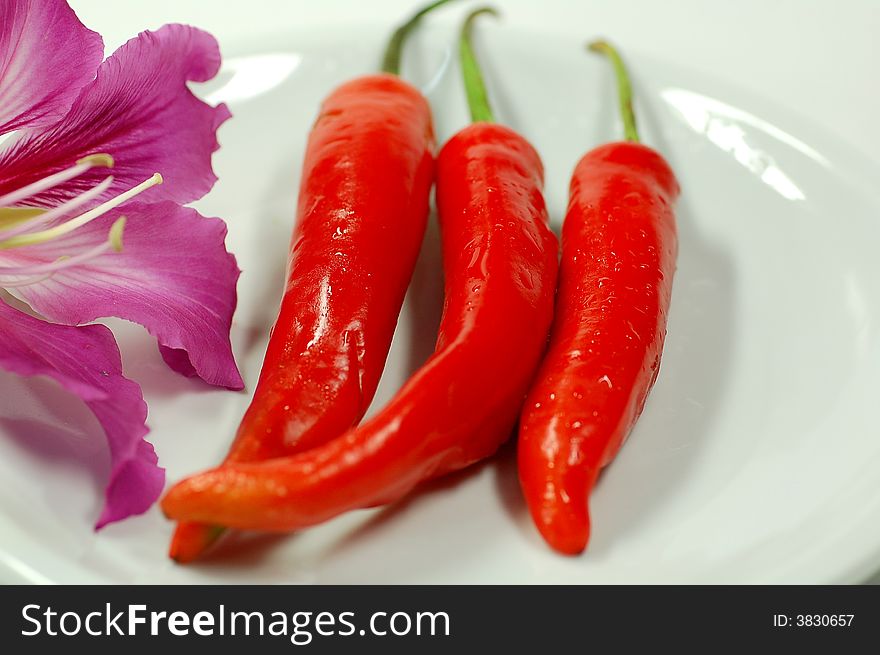 Three red chilies on the plate and a flower.