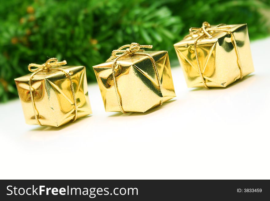 Golden christmas gift boxes isolated with a defucused leaf of evergreen on background