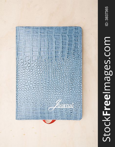 Cover of a light blue lizard skin journal note book book photographed directly above sitting on a wood table. Cover of a light blue lizard skin journal note book book photographed directly above sitting on a wood table.