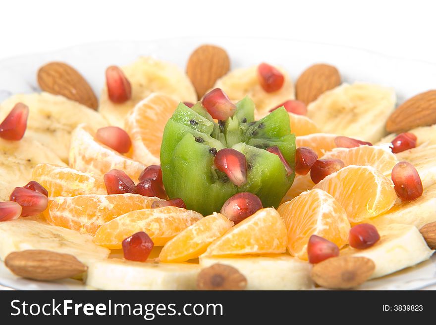 Delicious fruit salad made of kiwi, tangerines, bananas, almonds and pomegranate on white round plate isolated on white. Delicious fruit salad made of kiwi, tangerines, bananas, almonds and pomegranate on white round plate isolated on white