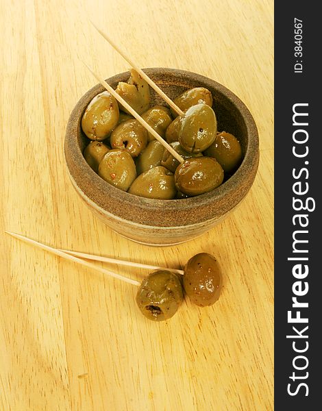 A bowl of olives with cocktail sticks on a wooden board