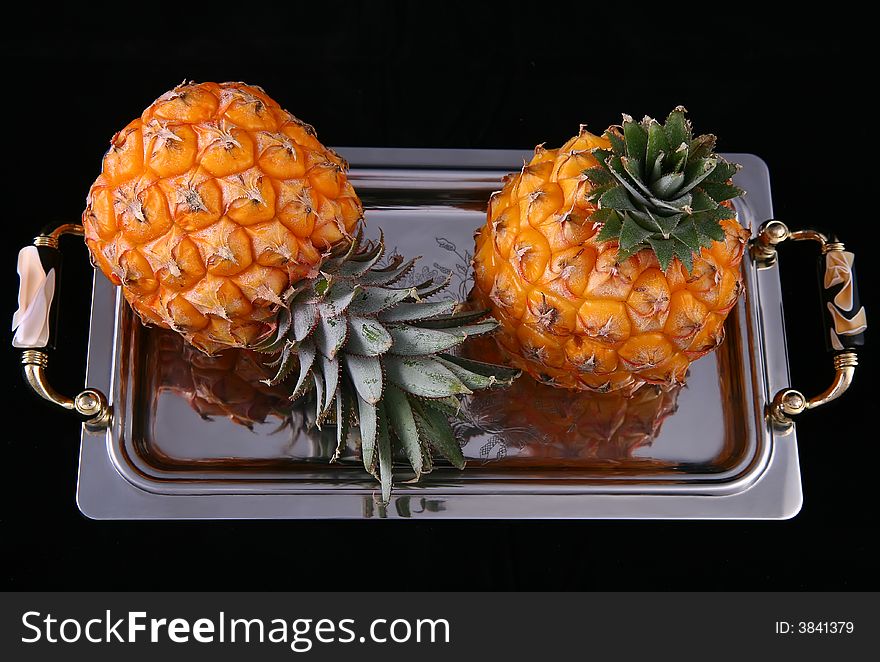 Two pineapples on the tray against black background