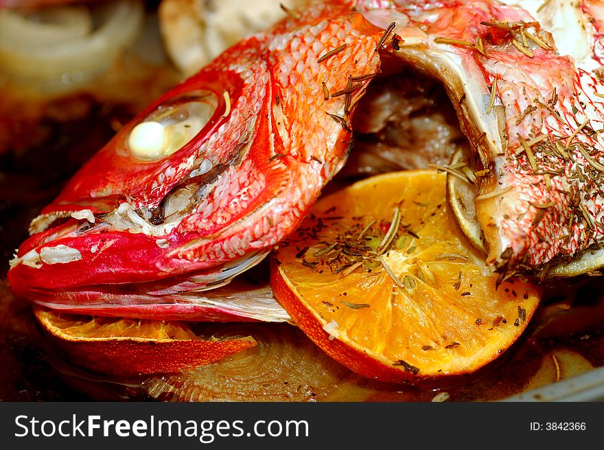 Close up image of a baked red snapper head with orange slices