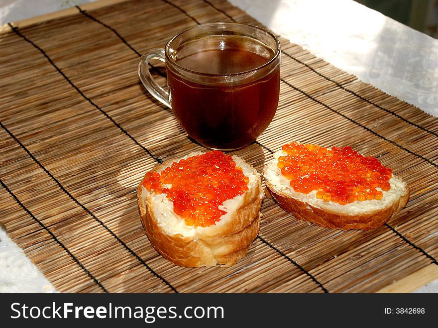 Breakfast - cup of coffee and two sandwiches with red caviar on sunlit bamboo matting