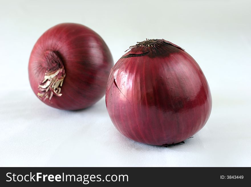 Two large, whole, raw purple Dutch beauty onions on a white table top