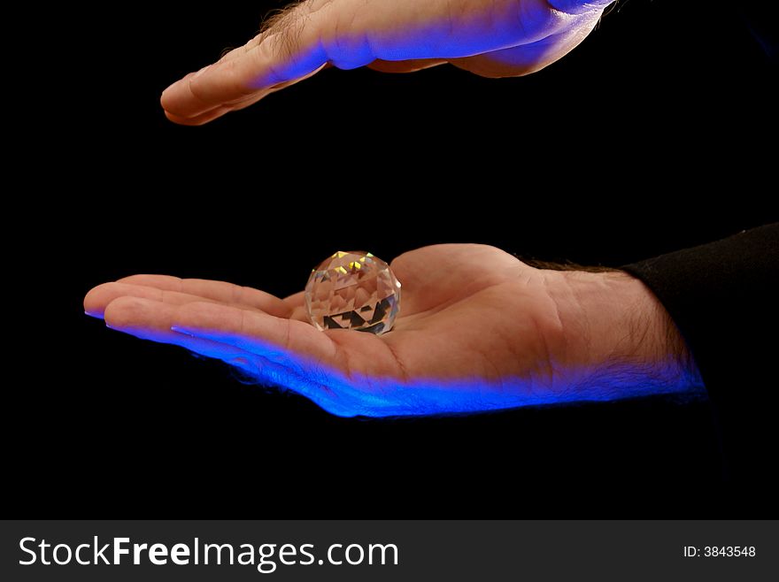Magician waving hand over faceted crystal, theatrical blue lighting illuminates the hands against a black background. Magician waving hand over faceted crystal, theatrical blue lighting illuminates the hands against a black background