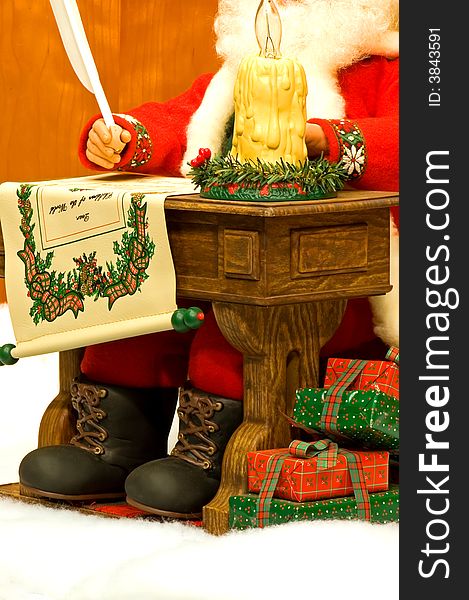 A view of a Santa Claus sitting at a small desk, writing a list of all the boys and girls who will get Christmas toys with Christmas presents piled at his feet. A view of a Santa Claus sitting at a small desk, writing a list of all the boys and girls who will get Christmas toys with Christmas presents piled at his feet.