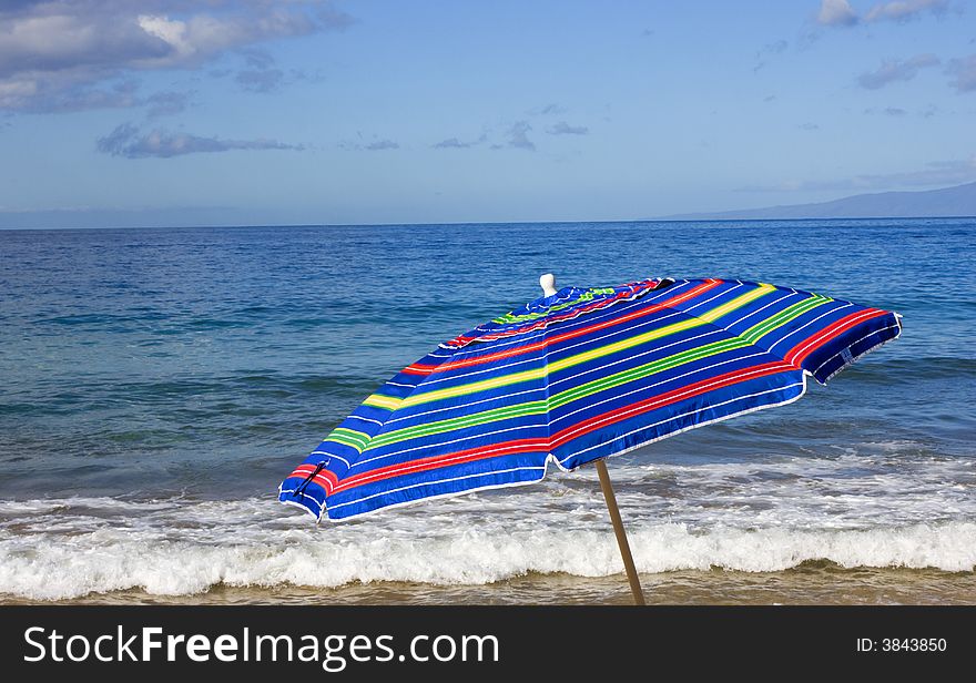 Blue ocean, blue sky, and a cheery striped umbrella at the beach. Blue ocean, blue sky, and a cheery striped umbrella at the beach.