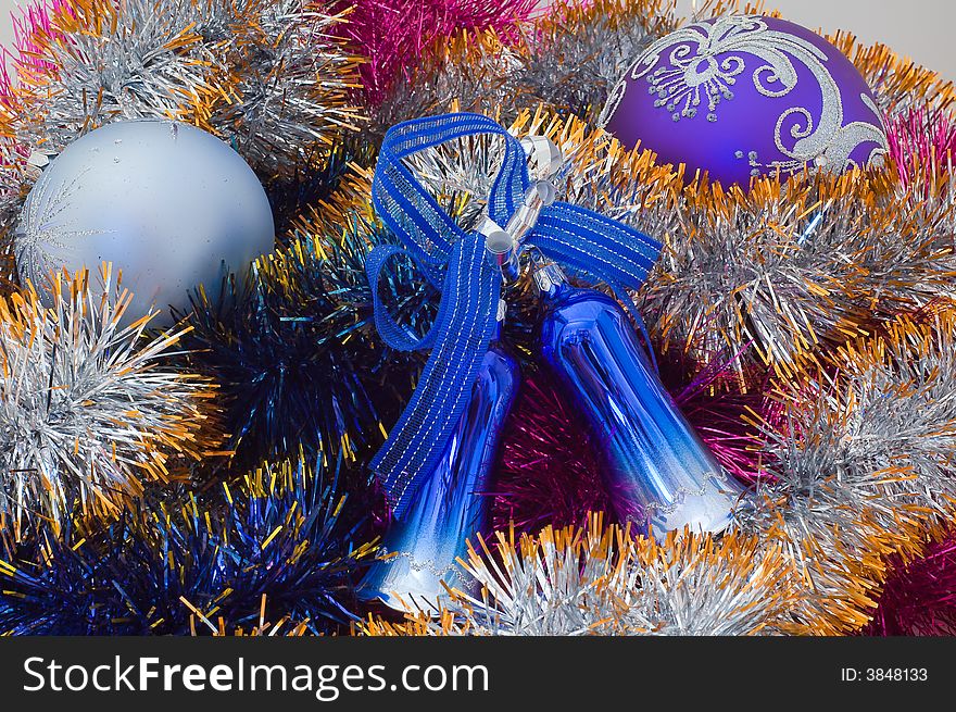 Photo of two coloured Christmas tree balls and bells at the middle of tinsel. Photo of two coloured Christmas tree balls and bells at the middle of tinsel