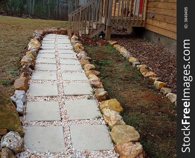 A stepping stone and pebble walkway surrounded by river rocks leading up to red front door and front porch.