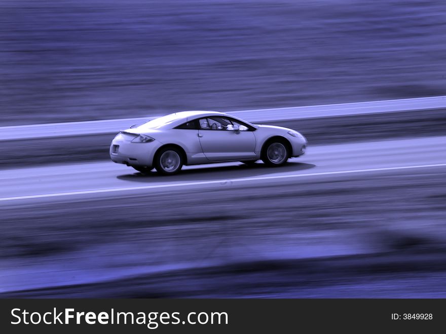 Two door sedan driving along road with blurred background