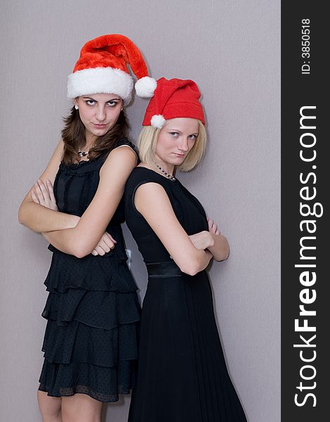 Two beautiful girls in red christmas caps and in black clothes threateningly look in a lens