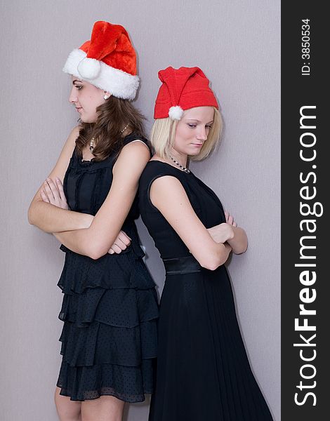 Two beautiful girls in red christmas caps and in black clothes cost a spin to the back and look in different directions
