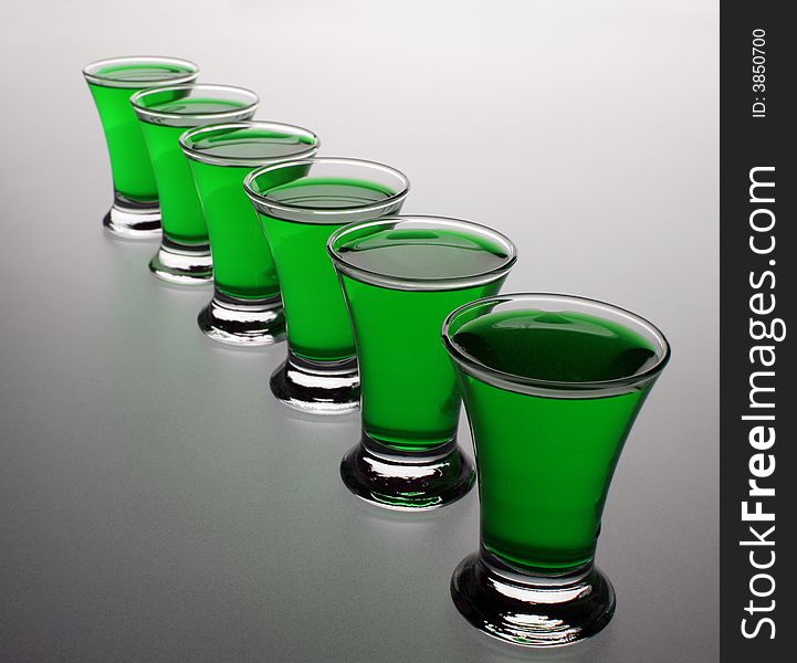 Photo of wine-glass with green liquid

 on the grey background. Photo of wine-glass with green liquid

 on the grey background