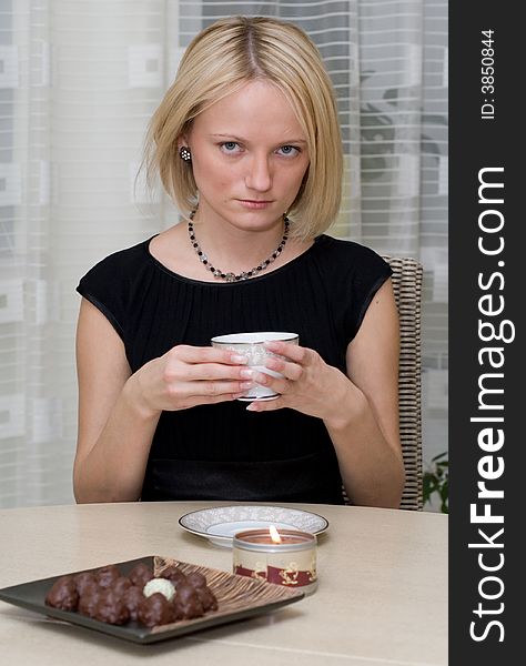 A beautiful woman in black clothes at the table has coffee