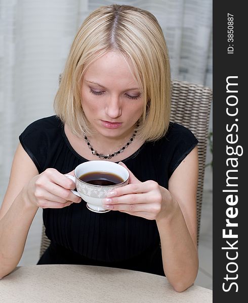 A beautiful woman in black clothes at the table has coffee