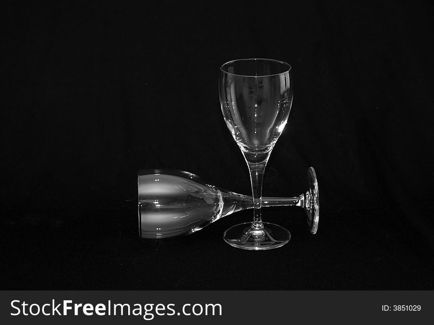 Thin wine glasses againt a black background, one laying down. Thin wine glasses againt a black background, one laying down