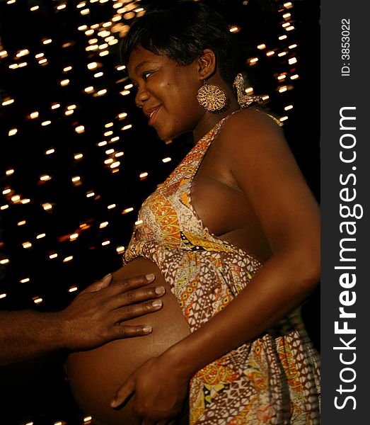 A hand of african american man touching his wife's belly with night bulbs setting on the background. the camera was moved to create moving background lights but the main subject was in focus. A hand of african american man touching his wife's belly with night bulbs setting on the background. the camera was moved to create moving background lights but the main subject was in focus