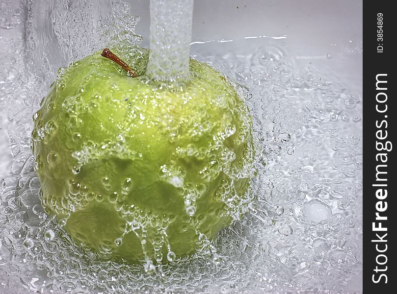 Green apple under running water in the sink. Green apple under running water in the sink