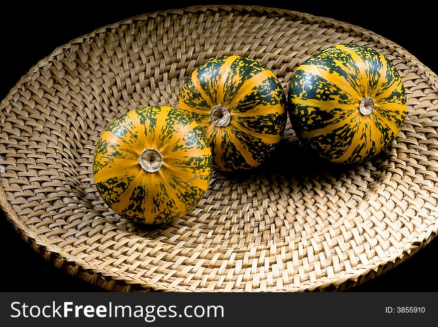 Three dark green-orange striped pumpkins placed on wickerwork plate. Three dark green-orange striped pumpkins placed on wickerwork plate