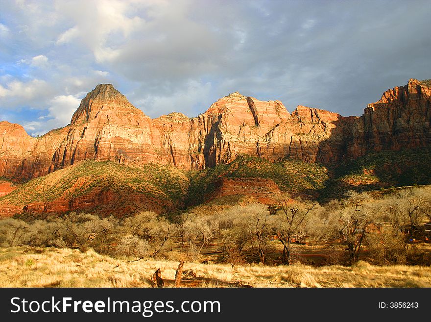 Late afternoon sunshine illuminating red sandstone cliffs of Zion National Park, Utah, with blue sky and clouds in background