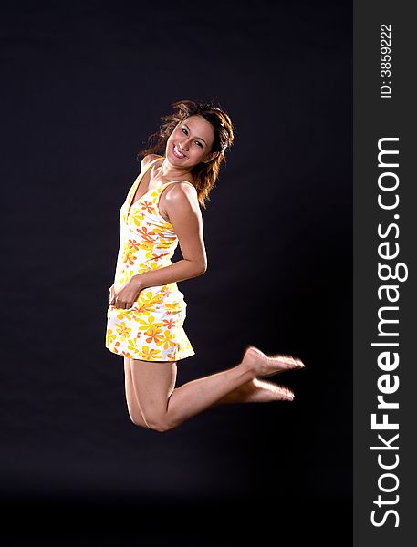 A Happy girl in yellow dress jumping joyfully on a black background. A Happy girl in yellow dress jumping joyfully on a black background