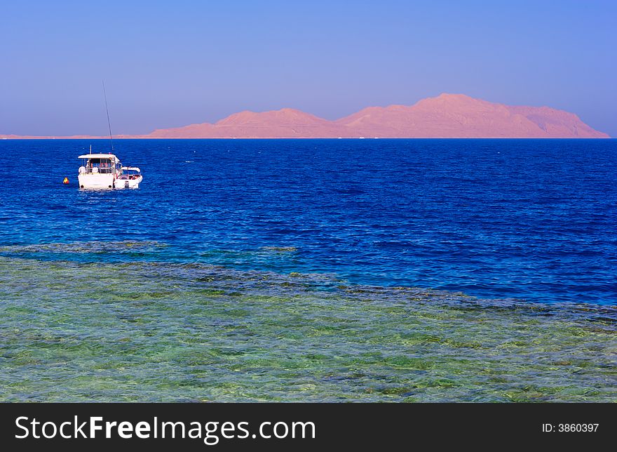 Rocky island in the sea with white boat