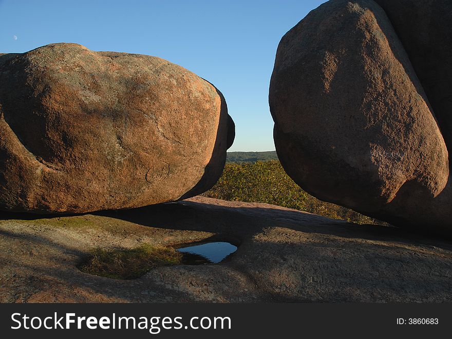 Two boulders with blue sky and the moon in the background.