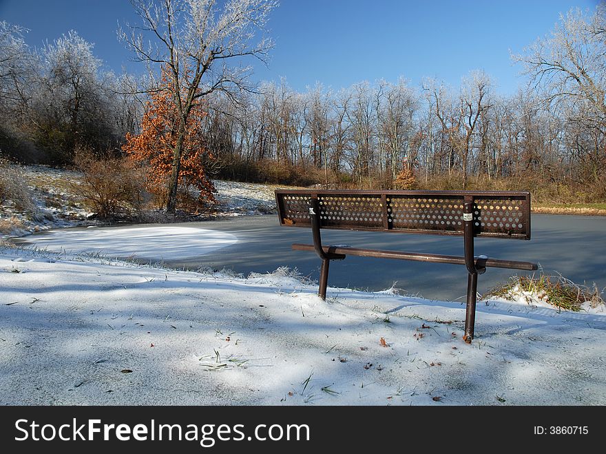A park bench overlooks a frozen pond on a sunny winter day. A park bench overlooks a frozen pond on a sunny winter day.