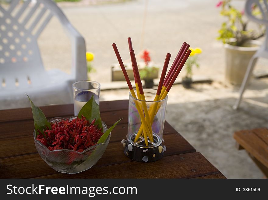 A glass of red and yellow chopsticks and red flowers on a table